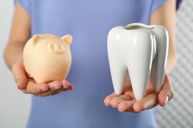 Photo of Woman holding ceramic model of tooth and piggy bank on light background, closeup. Expensive treatment