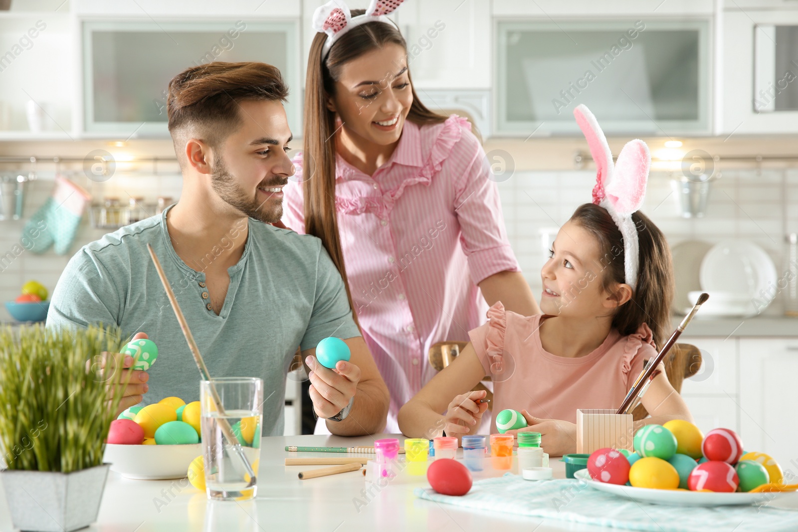 Photo of Father, mother and daughter painting Easter eggs in kitchen