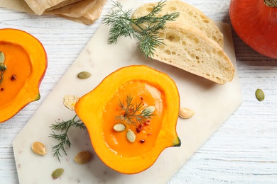 Photo of Tasty cream soup in pumpkin halves on white wooden table, flat lay