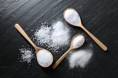 Photo of Organic salt in spoons on black table, flat lay