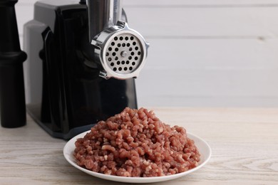 Photo of Electric meat grinder with beef mince on white wooden table. Space for text