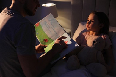 Photo of Father reading bedtime story to his daughter at home