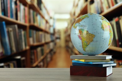 Image of Globe and books on wooden table in library. Space for text