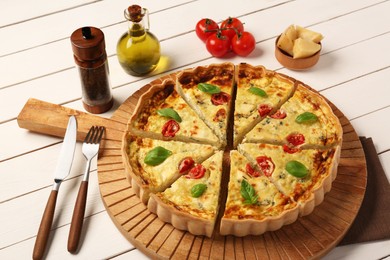 Photo of Delicious homemade cheese quiche, ingredients and cutlery on white wooden table