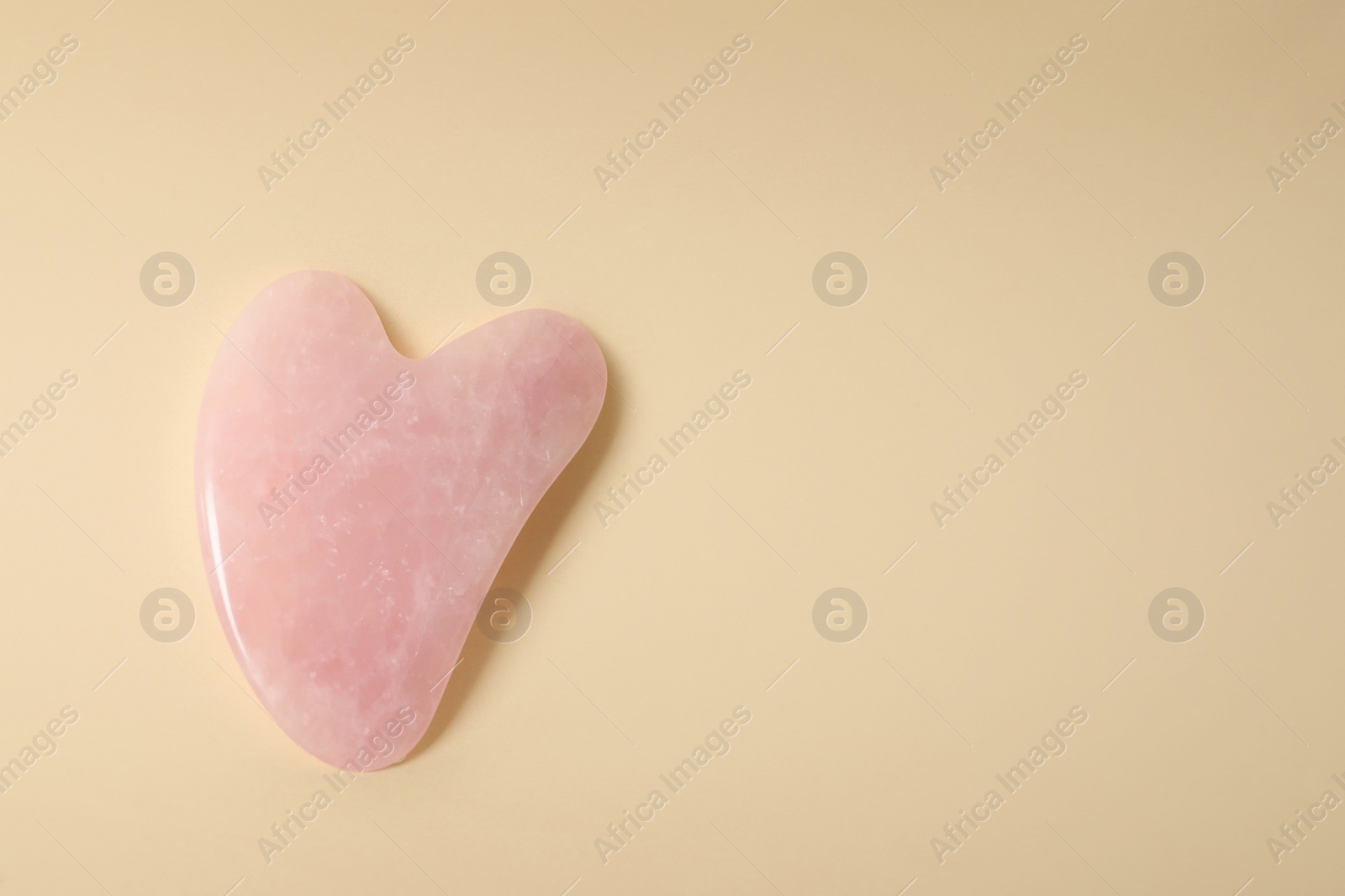 Photo of Rose quartz gua sha tool on beige background, top view. Space for text
