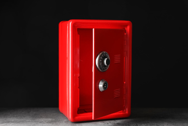 Photo of Red steel safe on grey stone table against black background