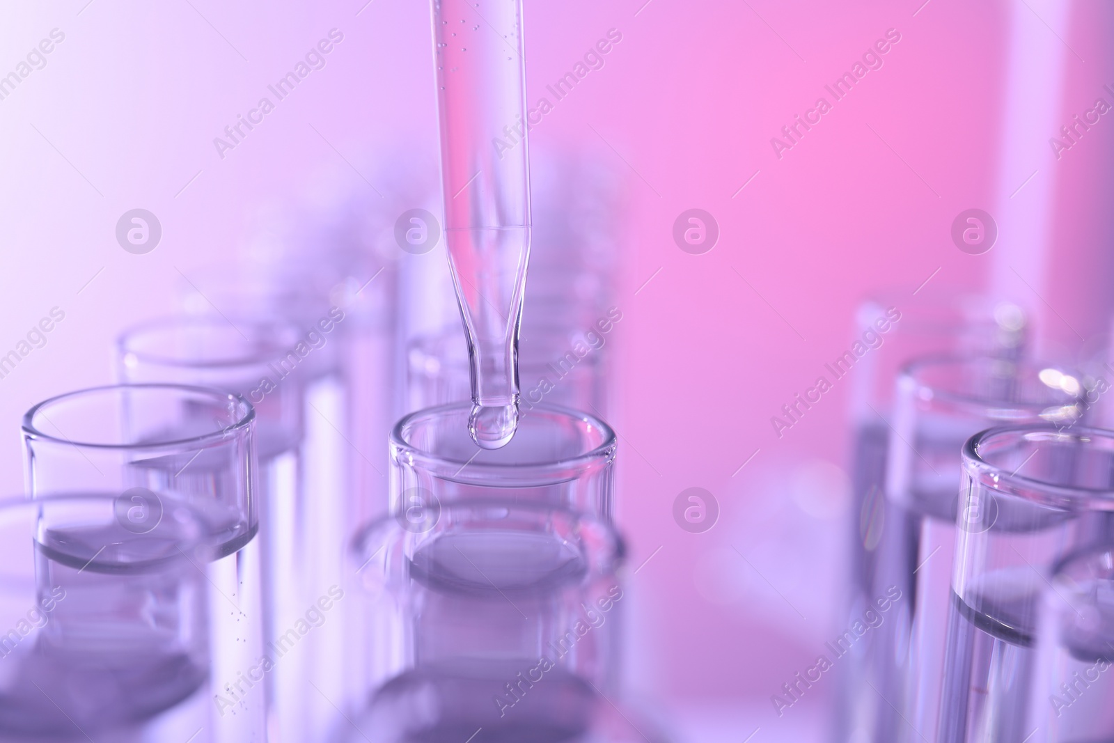 Photo of Dripping liquid from pipette into test tube on color background, closeup