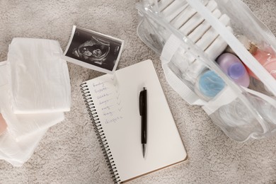 Flat lay composition with baby stuff, list and ultrasound scan on beige carpet