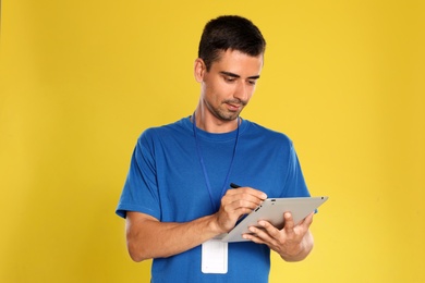 Photo of Happy young courier with tablet on yellow background