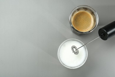 Photo of Mini mixer (milk frother), whipped milk and coffee in glasses on grey background, flat lay. Space for text