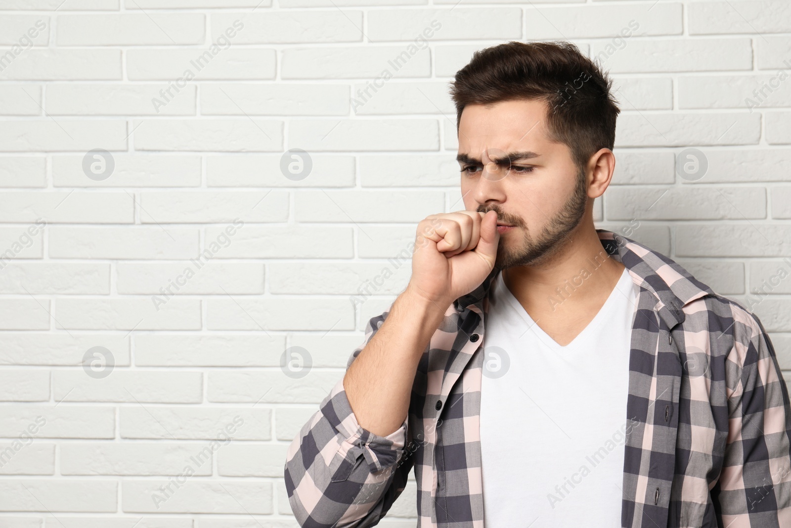 Photo of Handsome young man coughing near brick wall. Space for text