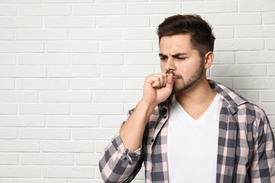 Handsome young man coughing near brick wall. Space for text