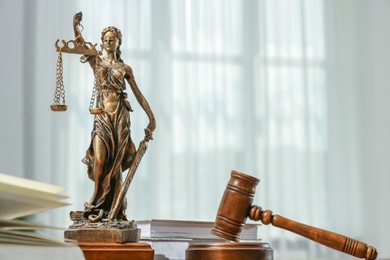 Photo of Figure of Lady Justice, gavel and books indoors, space for text. Symbol of fair treatment under law