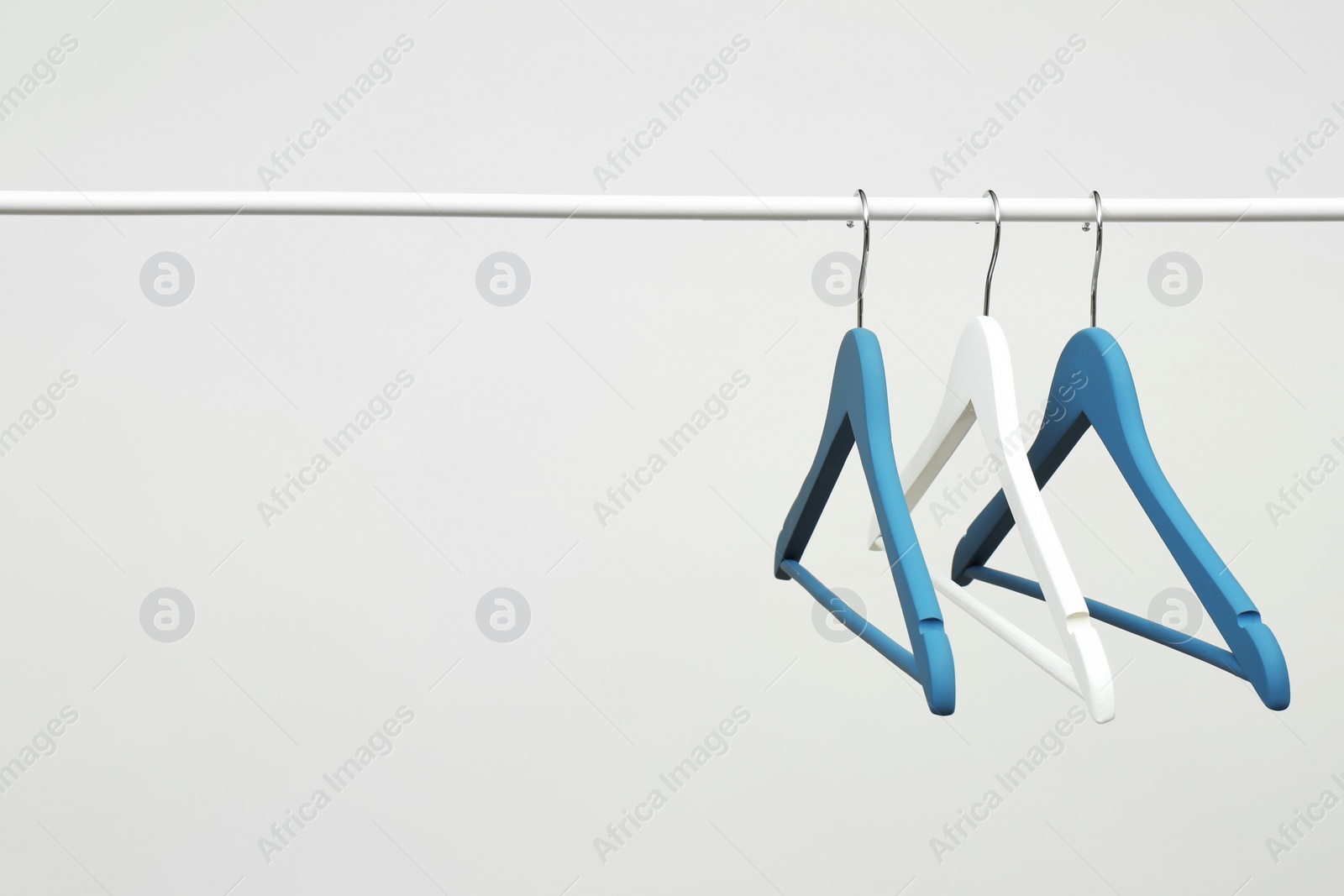 Photo of Empty clothes hangers on metal rail against light background. Space for text