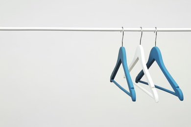 Empty clothes hangers on metal rail against light background. Space for text