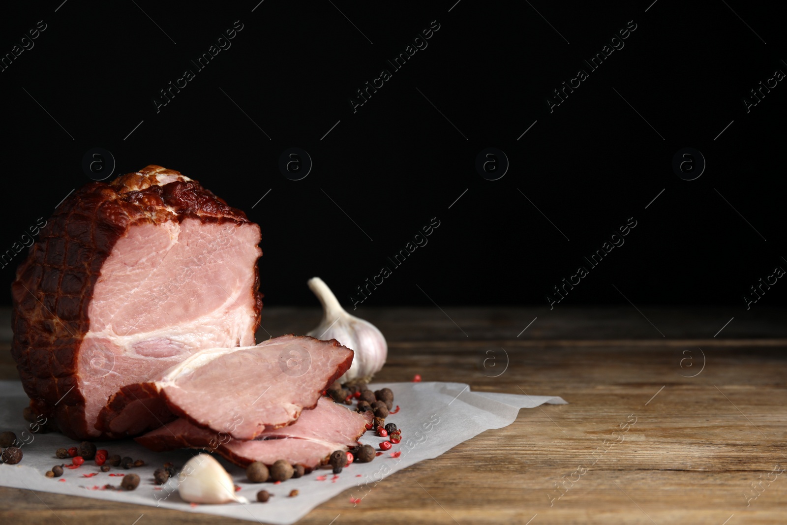 Photo of Cut delicious ham, spices and garlic on wooden table, space for text