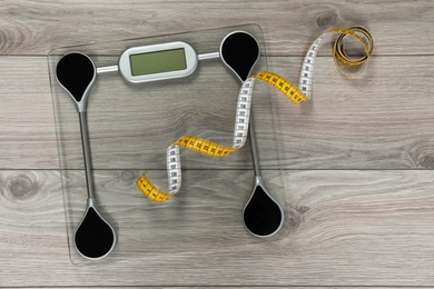 Photo of Scales and measuring tape on wooden background, top view. Weight loss