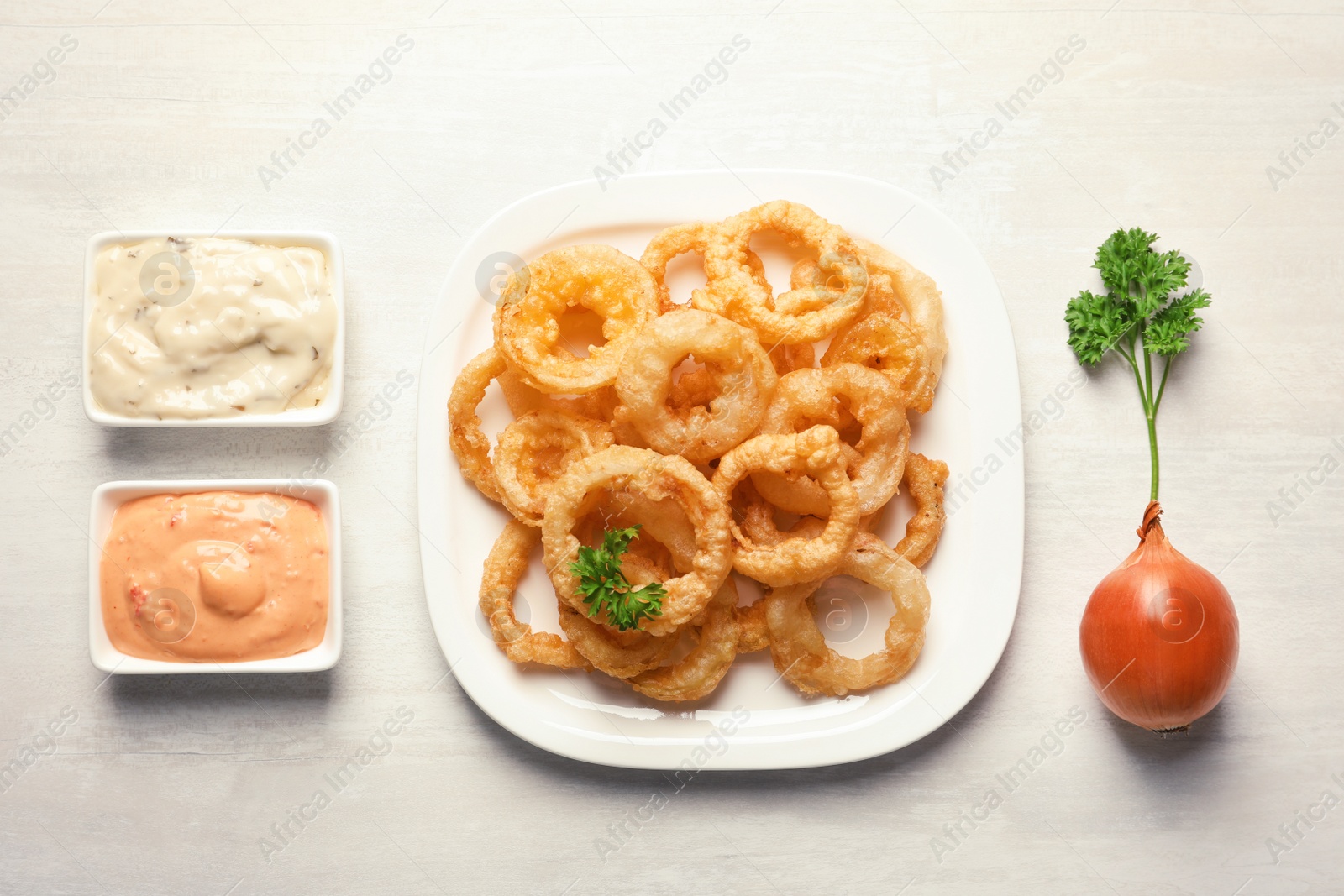 Photo of Plate with homemade crunchy fried onion rings and sauces on light background, top view