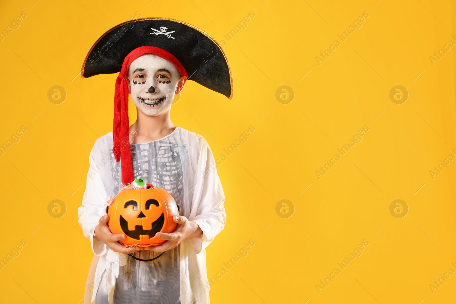 Photo of Cute little boy with pumpkin candy bucket wearing Halloween costume on yellow background. Space for text