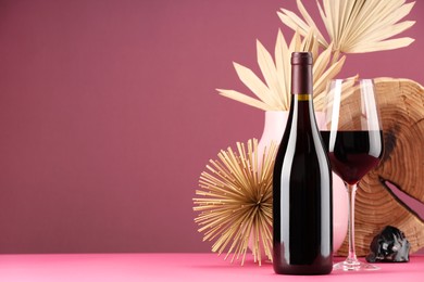 Photo of Stylish presentation of delicious red wine in bottle and glass on pink background. Space for text