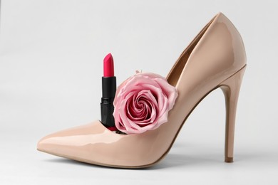 Photo of Beautiful pink lipstick, rose and beige high heeled shoe on white background