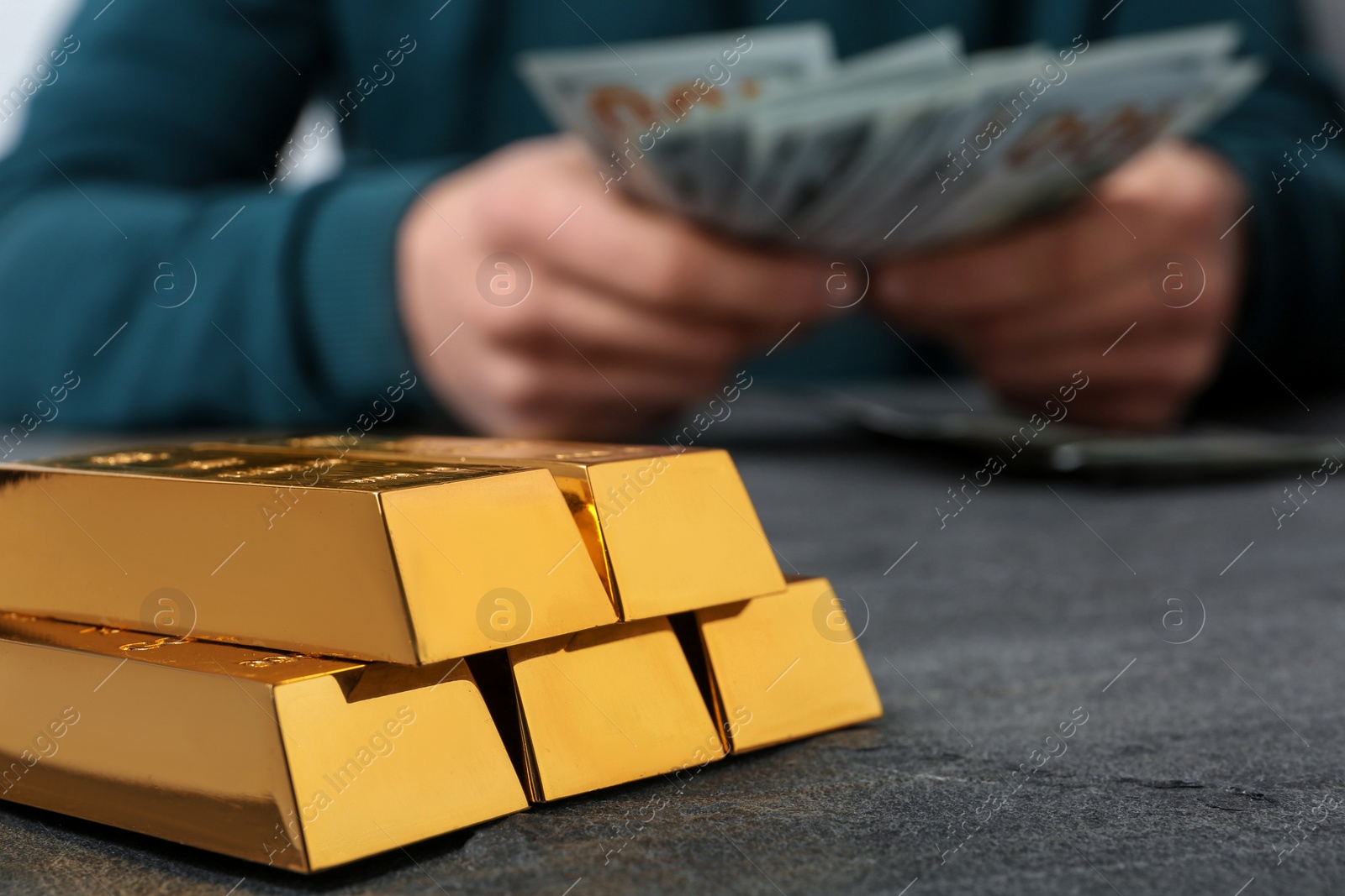 Photo of Stacked gold bars and man counting money at table, closeup. Space for text