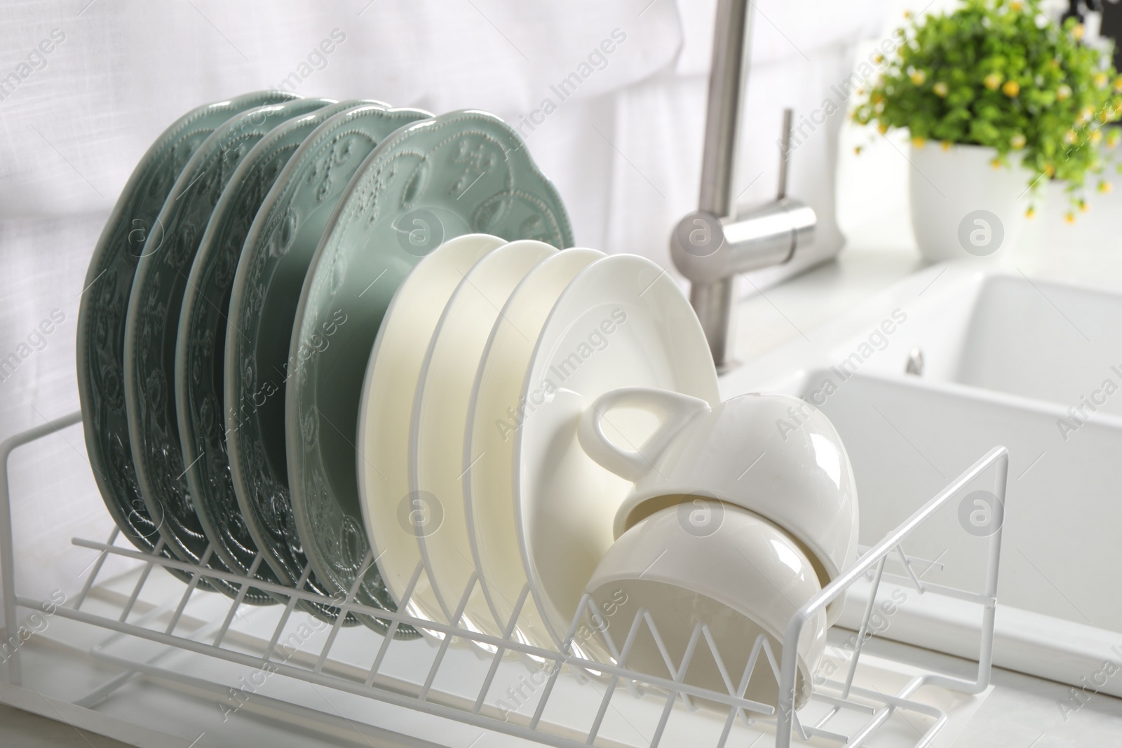 Photo of Drainer with different clean dishware and cups on white table in kitchen