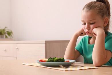 Photo of Cute little girl refusing to eat her breakfast at home, space for text