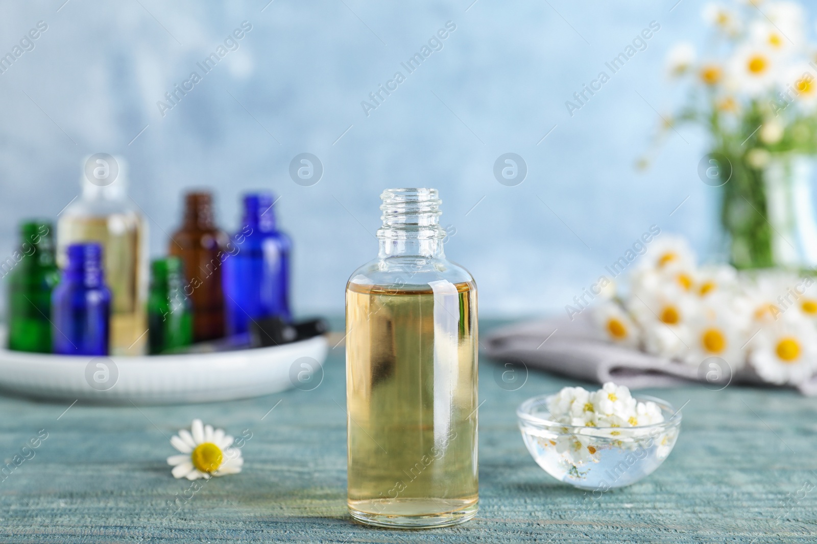 Photo of Bottle of essential oil, bowl and flowers table against color background