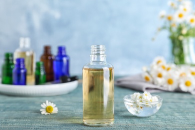 Photo of Bottle of essential oil, bowl and flowers table against color background