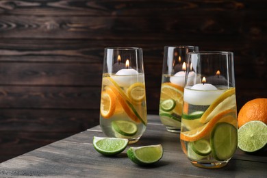 Candles and fruit slices in glass holders with liquid on wooden table