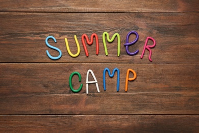 Photo of Text SUMMER CAMP made of modelling clay on wooden table, flat lay