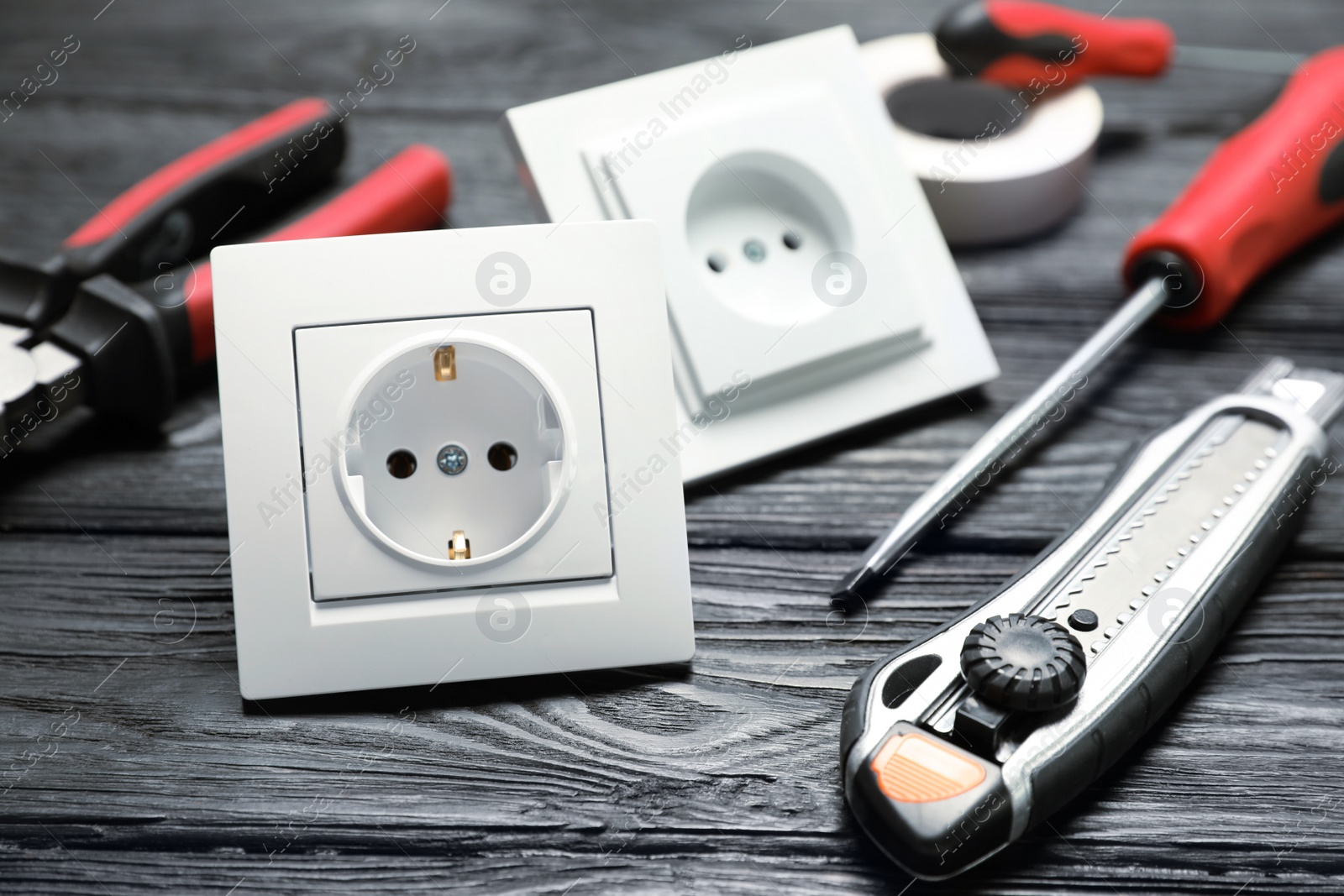 Photo of Power sockets and electrician's tools on black wooden table, closeup