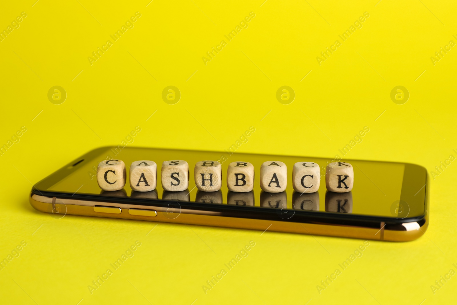 Photo of Word Cashback made with wooden cubes and smartphone on yellow background