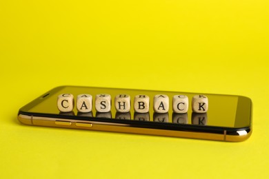 Word Cashback made with wooden cubes and smartphone on yellow background