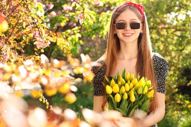 Photo of Beautiful teenage girl with bouquet of yellow tulips in park on sunny day