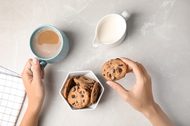 Photo of Woman holding tasty chocolate chip cookie and cup of coffee on light background, top view