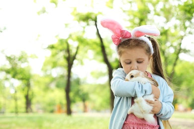 Photo of Little girl with adorable bunny outdoors on sunny day. Easter celebration