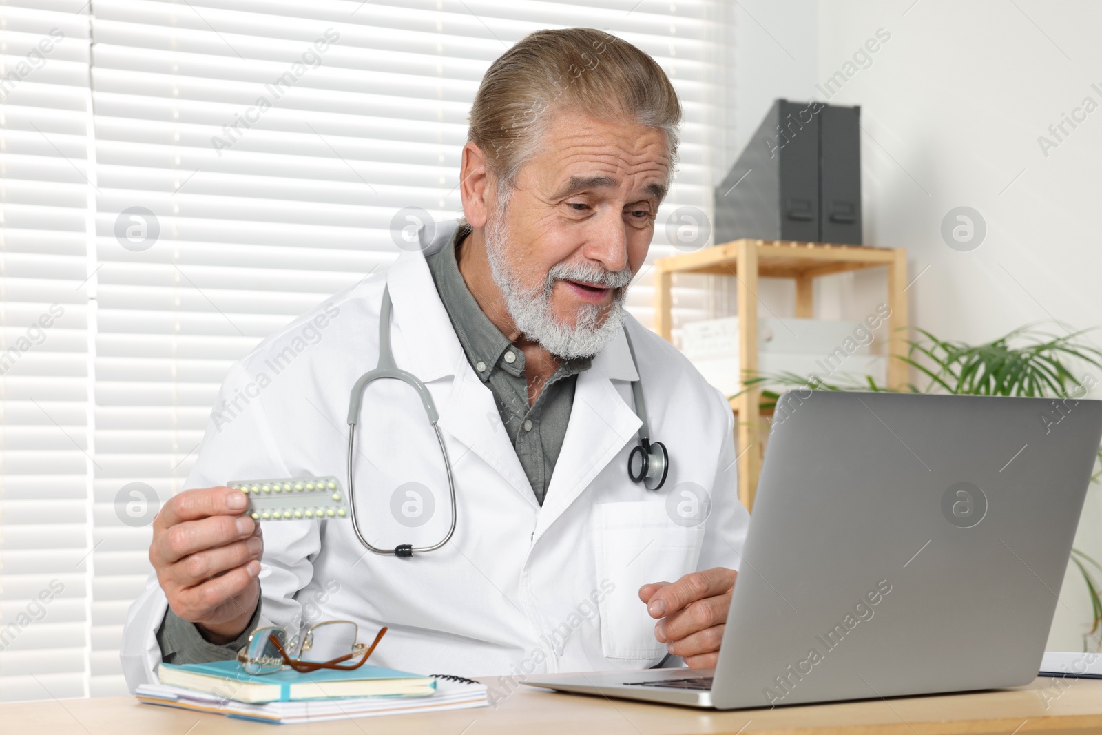 Photo of Happy senior doctor with laptop consulting patient at wooden desk in clinic. Online medicine