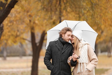 Photo of Young romantic couple with umbrella in park on autumn day