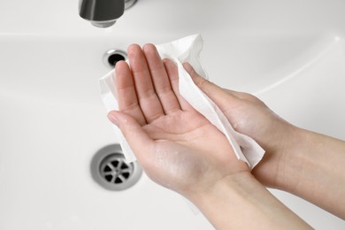 Woman wiping hands with paper towel near sink, closeup