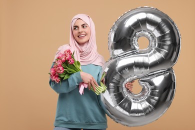 Photo of Happy Women's Day. Woman in hijab with beautiful bouquet and balloon in shape of number 8 on beige background