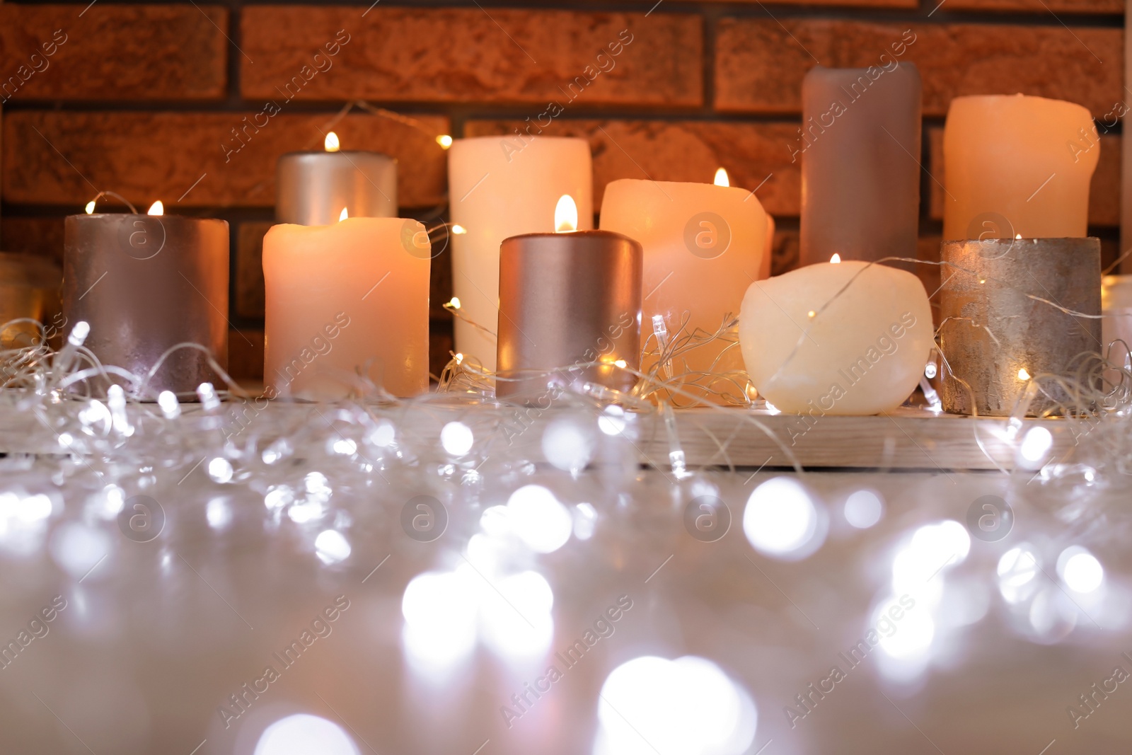 Photo of Burning candles and Christmas lights on floor indoors