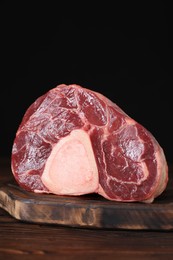 Photo of Piece of raw beef meat on wooden table against black background, closeup
