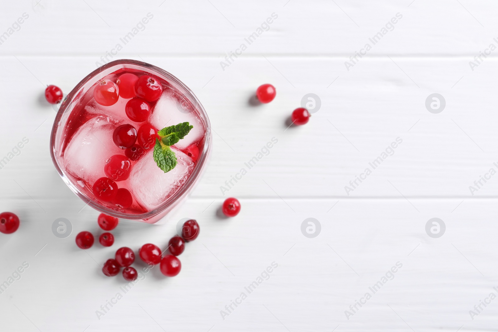 Photo of Tasty cranberry juice with ice cubes in glass and fresh berries on white wooden table, flat lay. Space for text