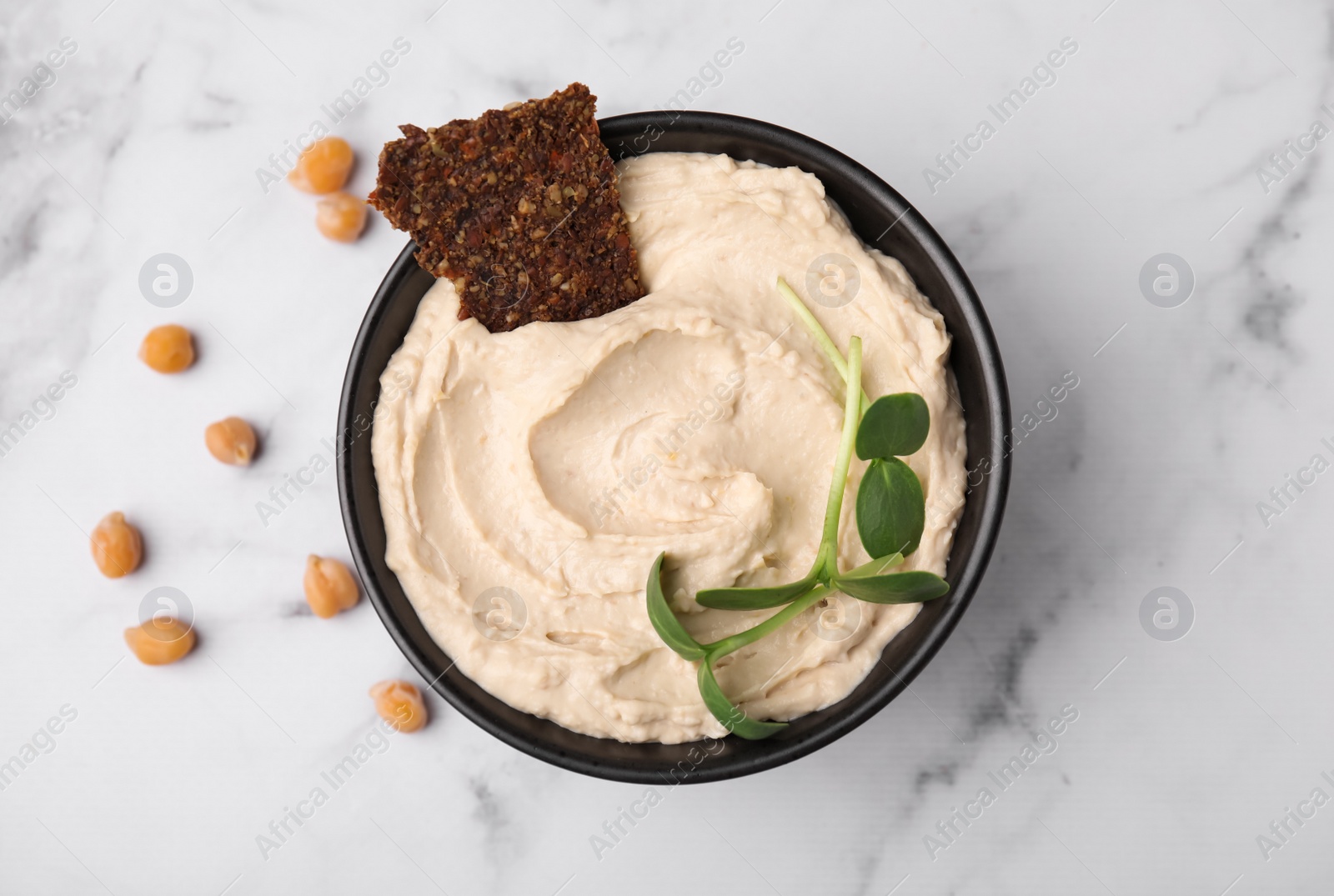 Photo of Bowl of delicious hummus with crispbread on white marble table, flat lay