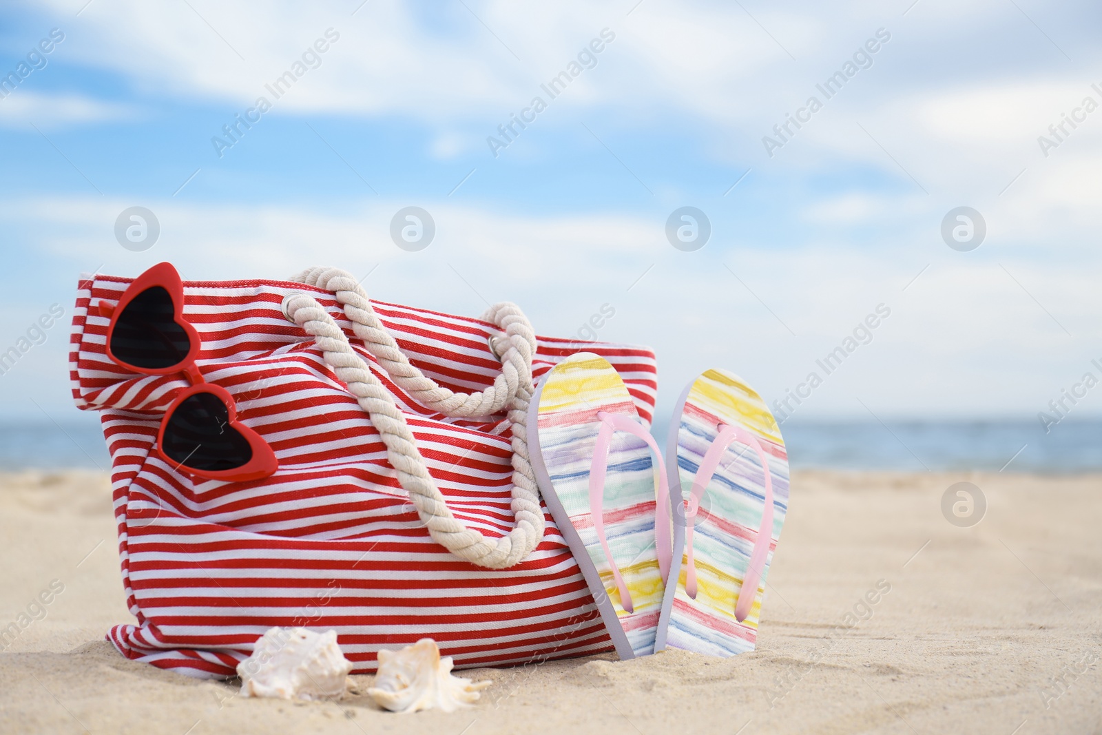 Photo of Different stylish beach objects and seashells on sand near sea