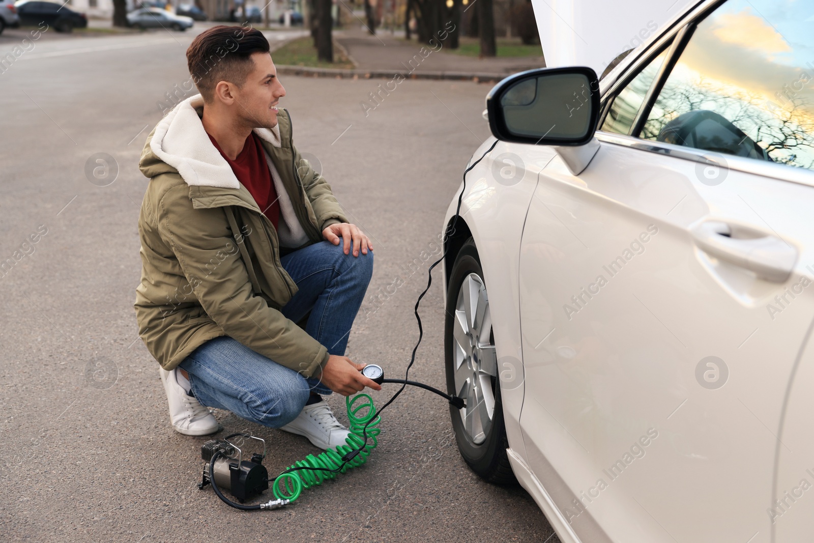 Photo of Handsome man inflating car tire with air compressor on street