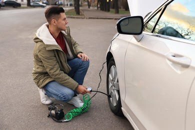 Handsome man inflating car tire with air compressor on street