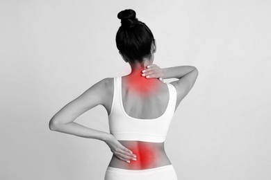 Woman suffering from back and neck pain on light background